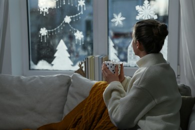 Photo of Woman with hot drink on sofa near beautifully decorated window at home