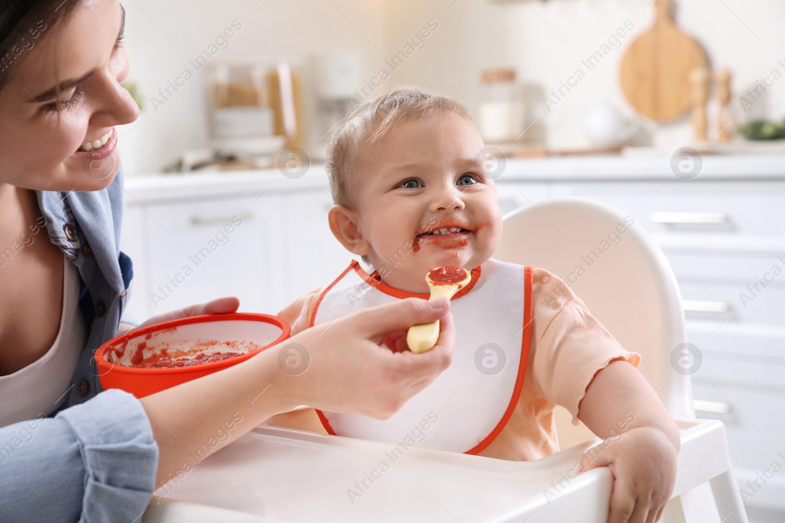 Photo of Mother feeding her cute little baby in kitchen