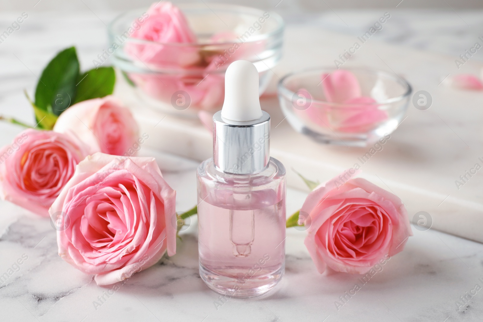 Photo of Bottle with rose essential oil and flowers on marble table