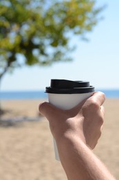 Photo of Woman with takeaway coffee cup on beach, closeup. Space for text