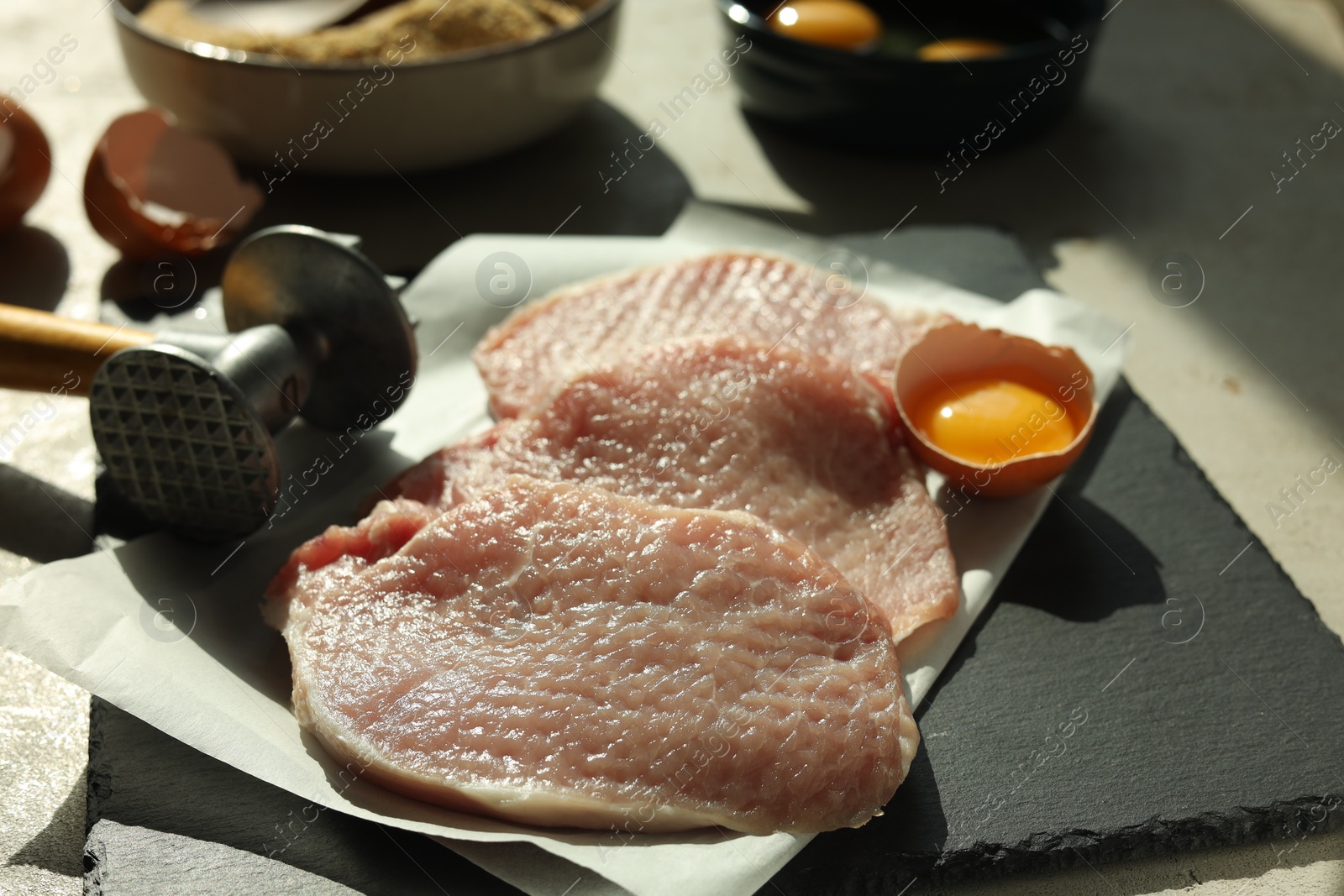 Photo of Cooking schnitzel. Raw pork chops, meat mallet and ingredients on grey table, closeup