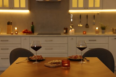 Photo of Glasses of wine, burning candle and food on wooden table in kitchen