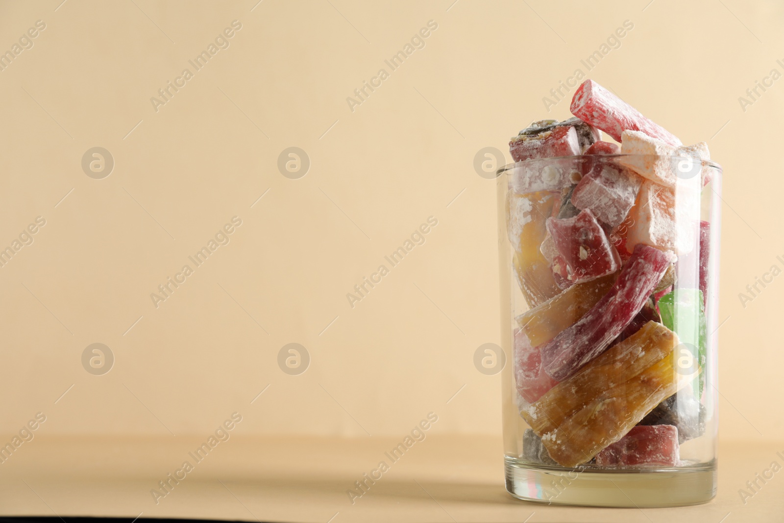 Photo of Delicious candies in glass on beige background, closeup. Space for text