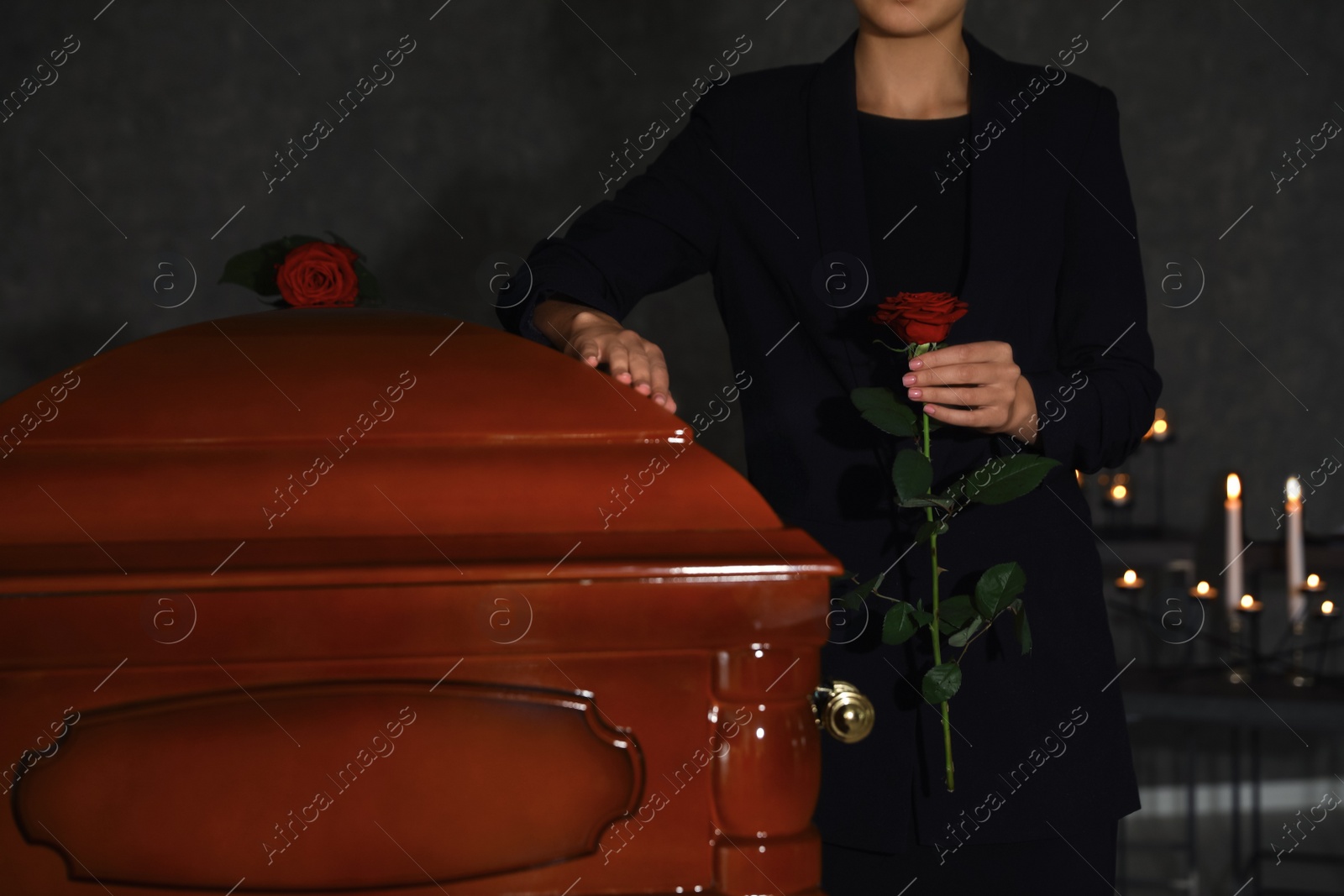 Photo of Young woman with red rose near casket in funeral home, closeup