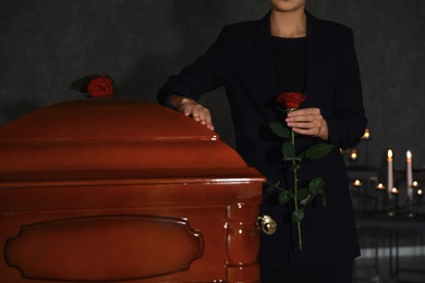 Young woman with red rose near casket in funeral home, closeup