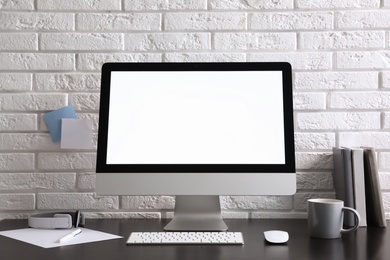 Comfortable workplace with modern computer on black table near white brick wall. Space for text