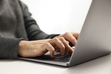 Photo of E-learning. Young man using laptop at white table, closeup