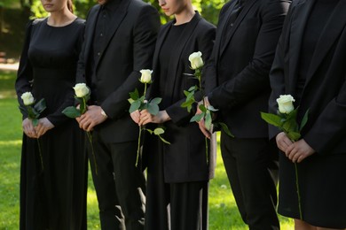 Photo of People in black clothes with white rose flowers outdoors, closeup. Funeral ceremony