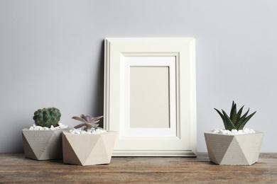 Blank frame and beautiful succulent plants on table against light background, space for design. Home decor