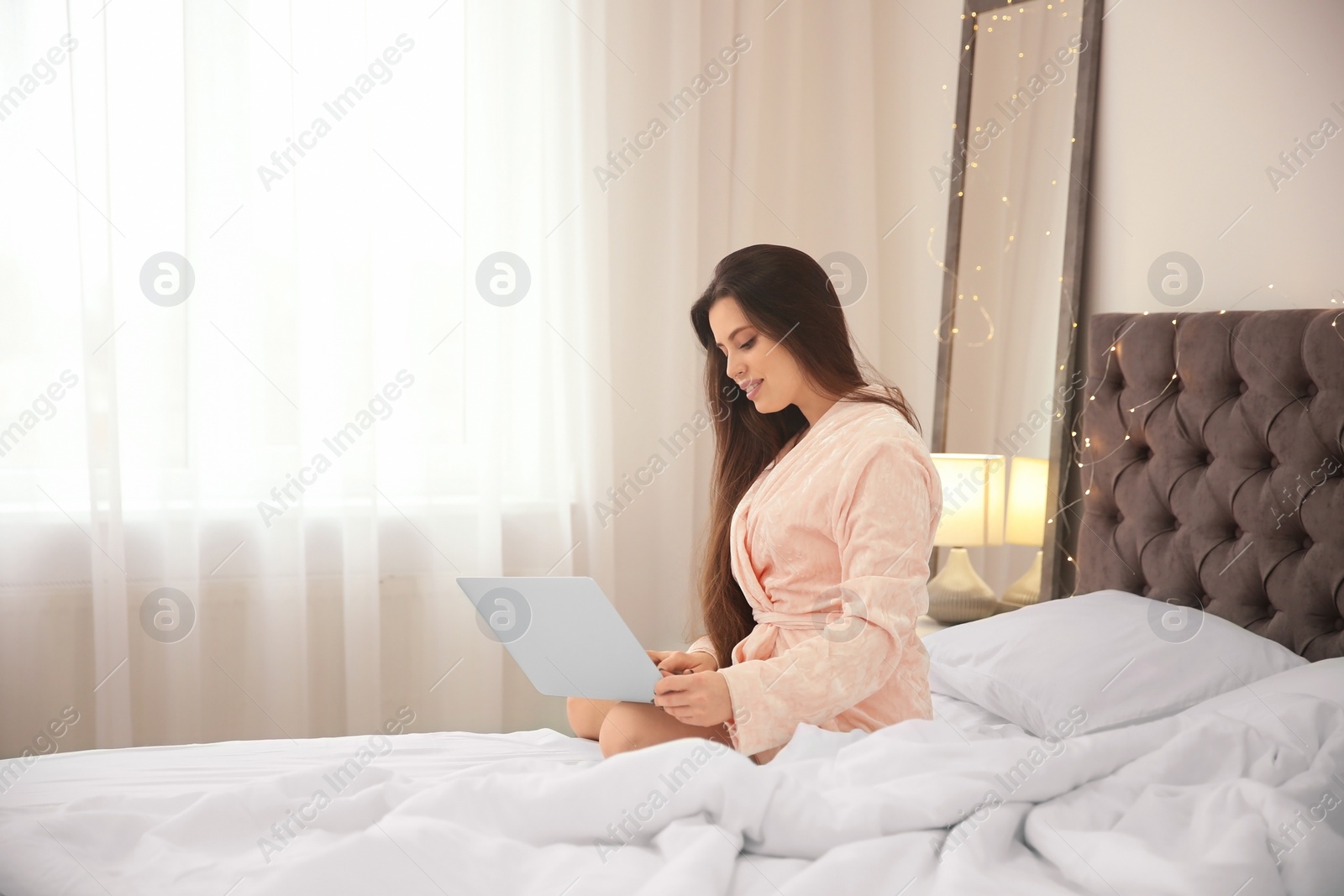 Photo of Young woman using laptop on bed in hotel room