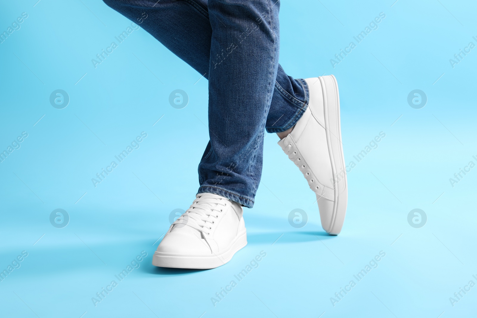 Photo of Man wearing stylish white sneakers on light blue background, closeup