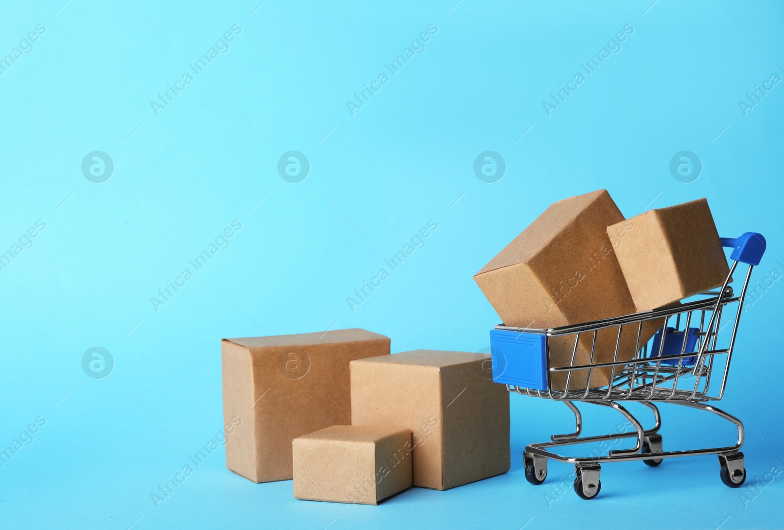 Photo of Shopping cart and boxes on light blue background, space for text. Logistics and wholesale concept