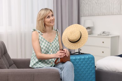 Photo of Smiling guest with bag relaxing on armchair in stylish hotel room
