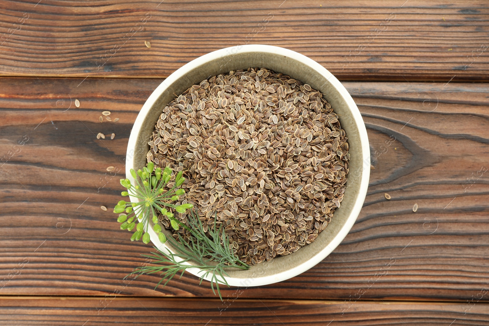 Photo of Bowl of dry seeds and fresh dill on wooden table, top view