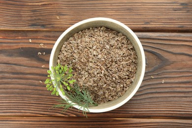 Photo of Bowl of dry seeds and fresh dill on wooden table, top view