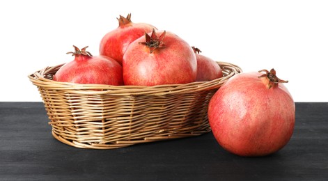 Fresh pomegranates in wicker basket on black wooden table against white background