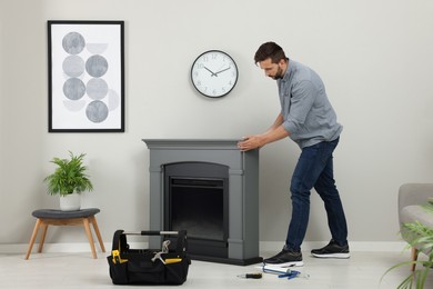 Man installing electric fireplace near wall in room