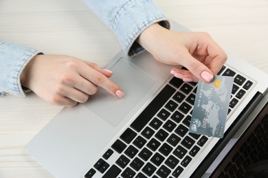 Online payment. Woman using credit card and laptop at white wooden table, above view