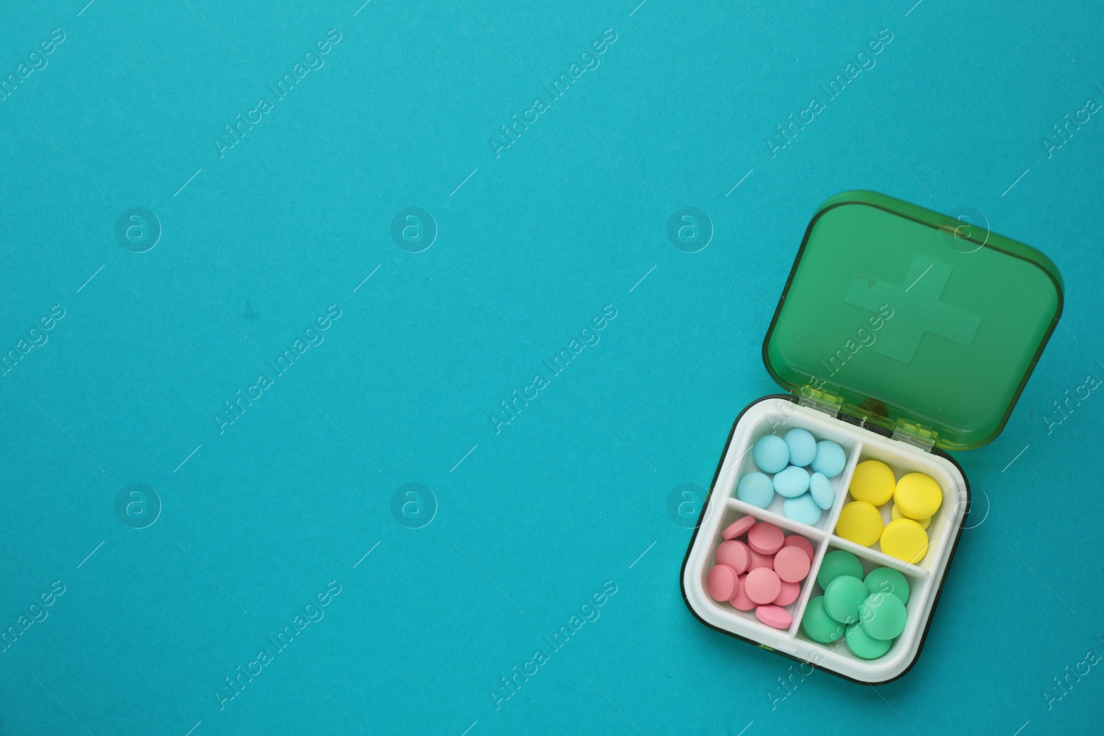 Photo of Plastic box with different pills on light blue background, top view. Space for text