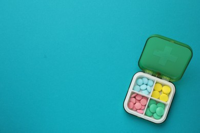 Plastic box with different pills on light blue background, top view. Space for text
