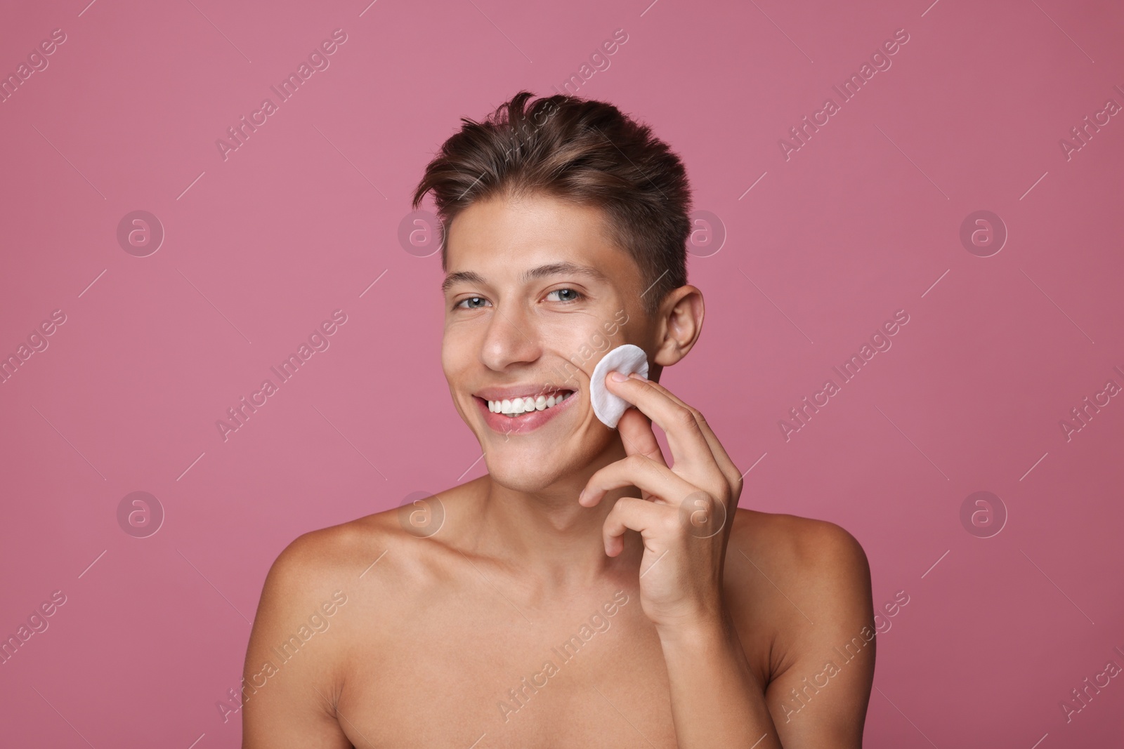 Photo of Handsome man cleaning face with cotton pad on pink background