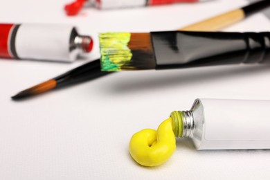 Photo of Tube with yellow oil paint and brushes on blank canvas, closeup
