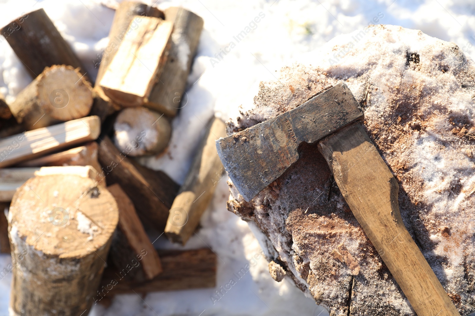 Photo of Metal axe on wooden log and pile of wood outdoors on sunny winter day, top view. Space for text