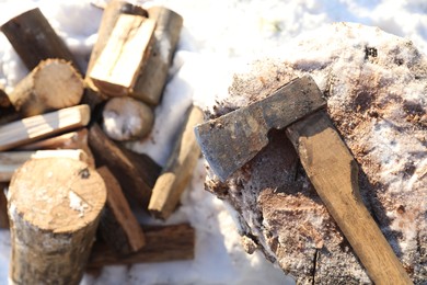 Metal axe on wooden log and pile of wood outdoors on sunny winter day, top view. Space for text
