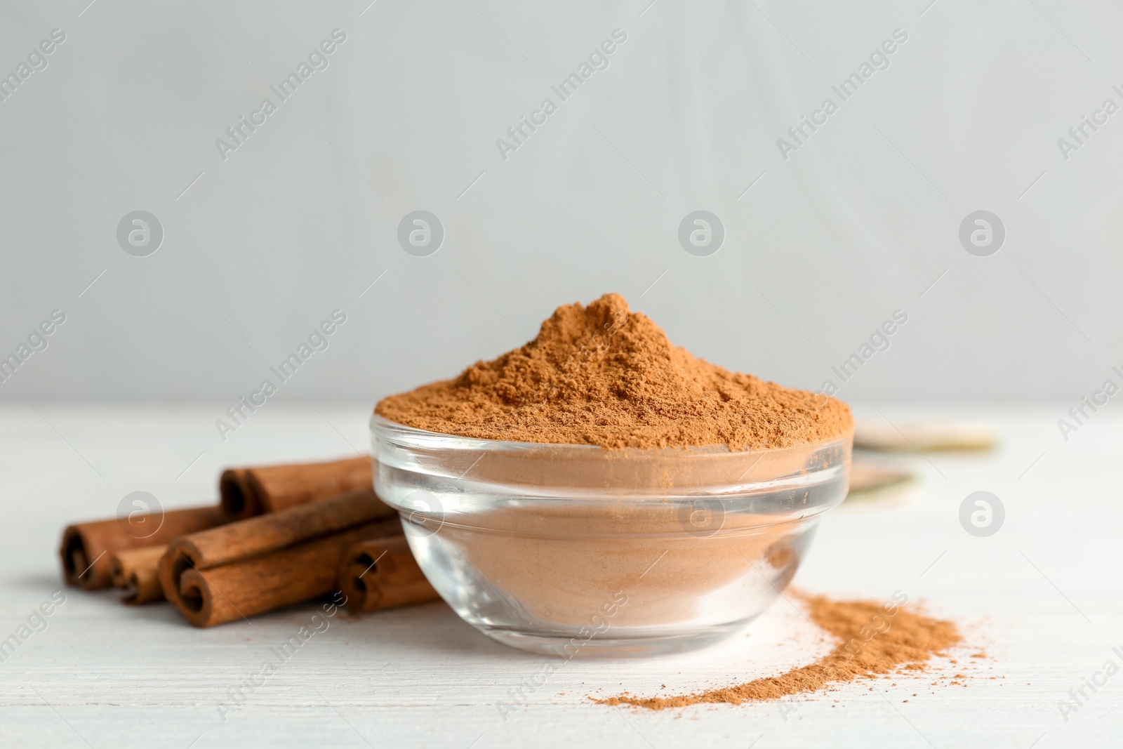 Photo of Bowl with aromatic cinnamon powder and sticks on wooden table