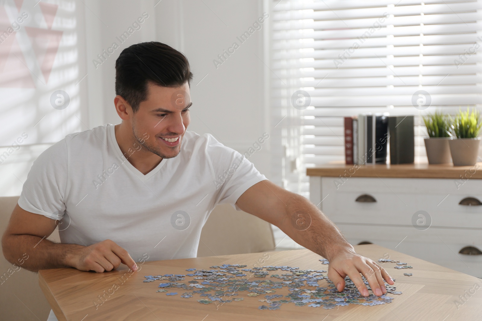 Photo of Man playing with puzzles at wooden table indoors