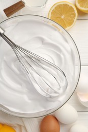 Bowl with whipped cream, whisk and ingredients on white wooden table, flat lay