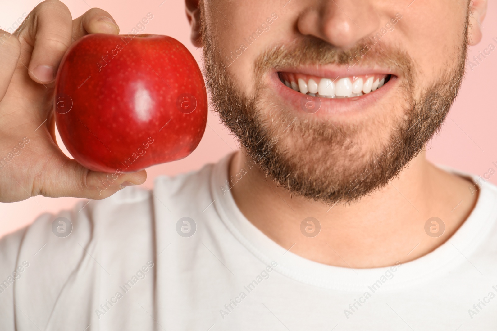 Photo of Young man with healthy teeth and apple on color background, closeup