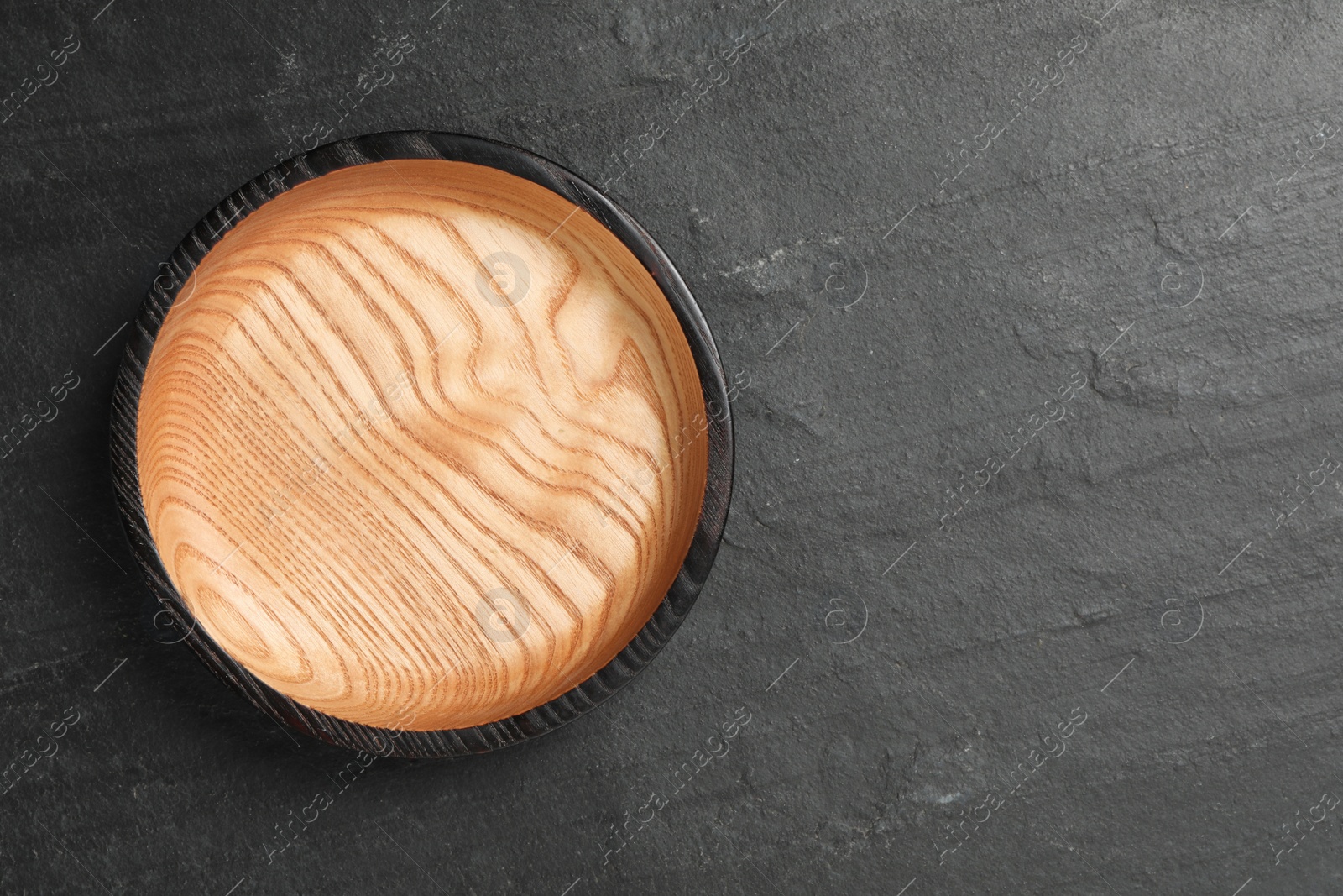 Photo of Empty clean wooden plate on black table, top view. Space for text