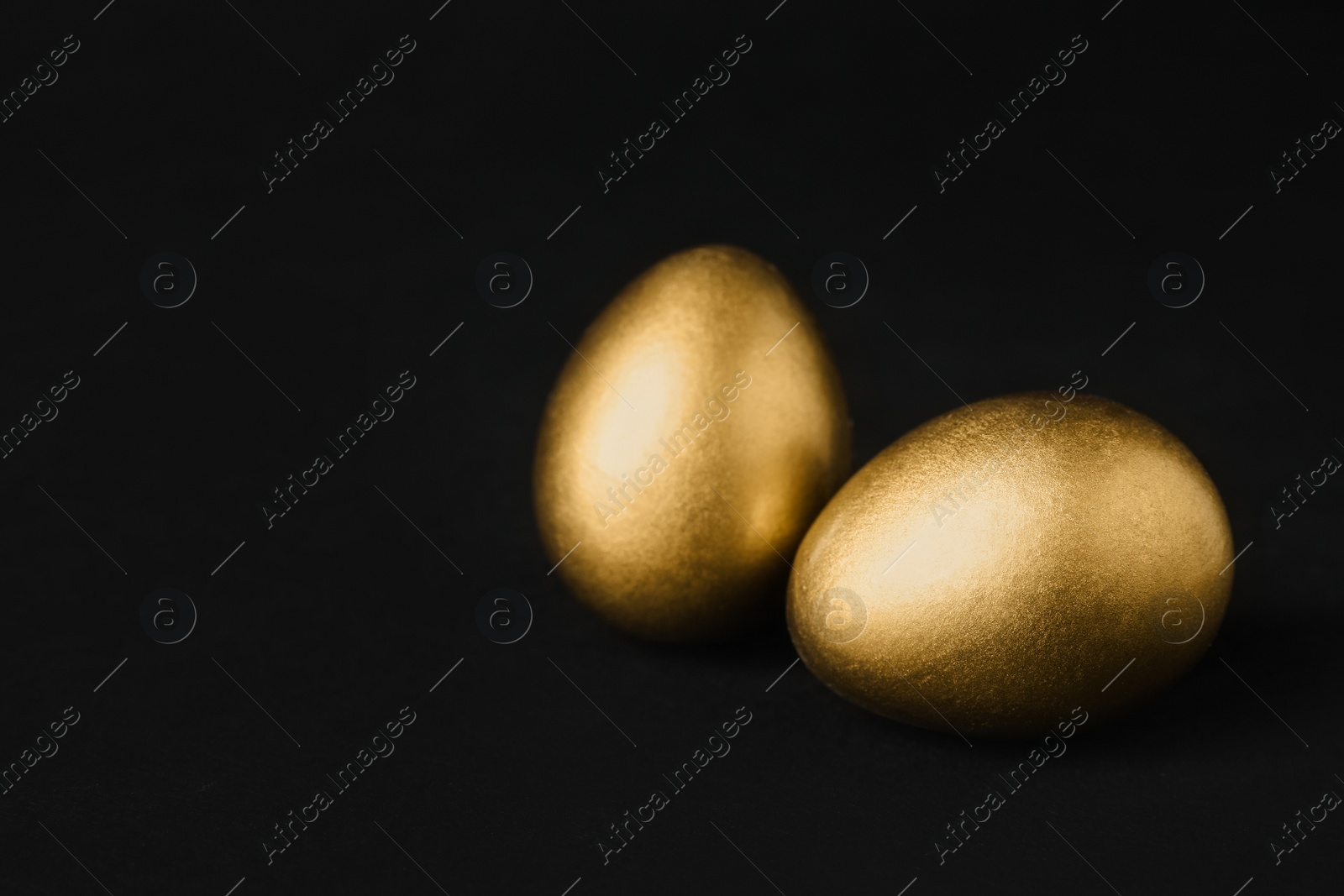 Photo of Shiny golden eggs on black background, space for text