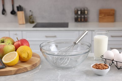 Metal whisk, bowl and different products on gray marble table in kitchen