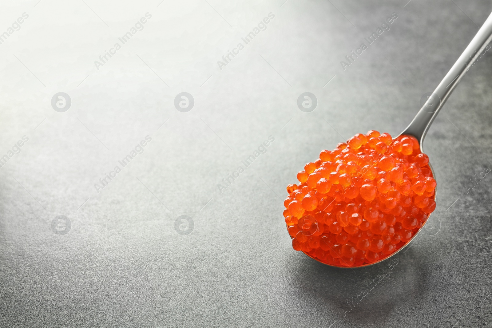 Photo of Spoon with delicious red caviar on grey background