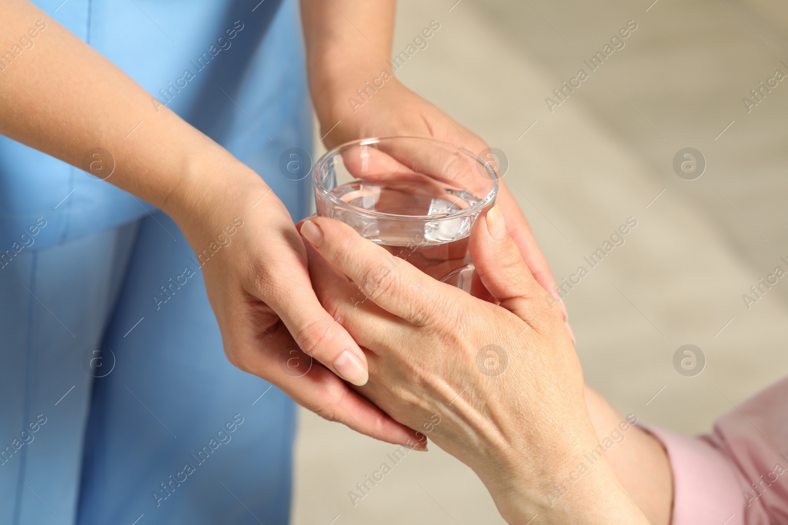 Photo of Caretaker giving glass of water to elderly woman indoors, closeup