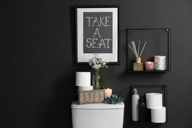 Photo of Decor elements, necessities and toilet bowl near black wall. Bathroom interior