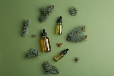 Three little bottles with essential oils and pine branches on color background, flat lay