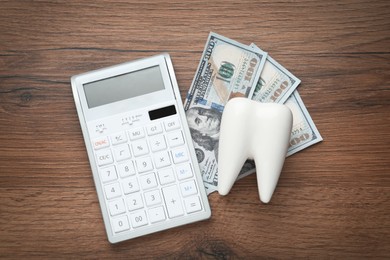 Ceramic model of tooth, dollar banknotes and calculator on wooden table, flat lay. Expensive treatment