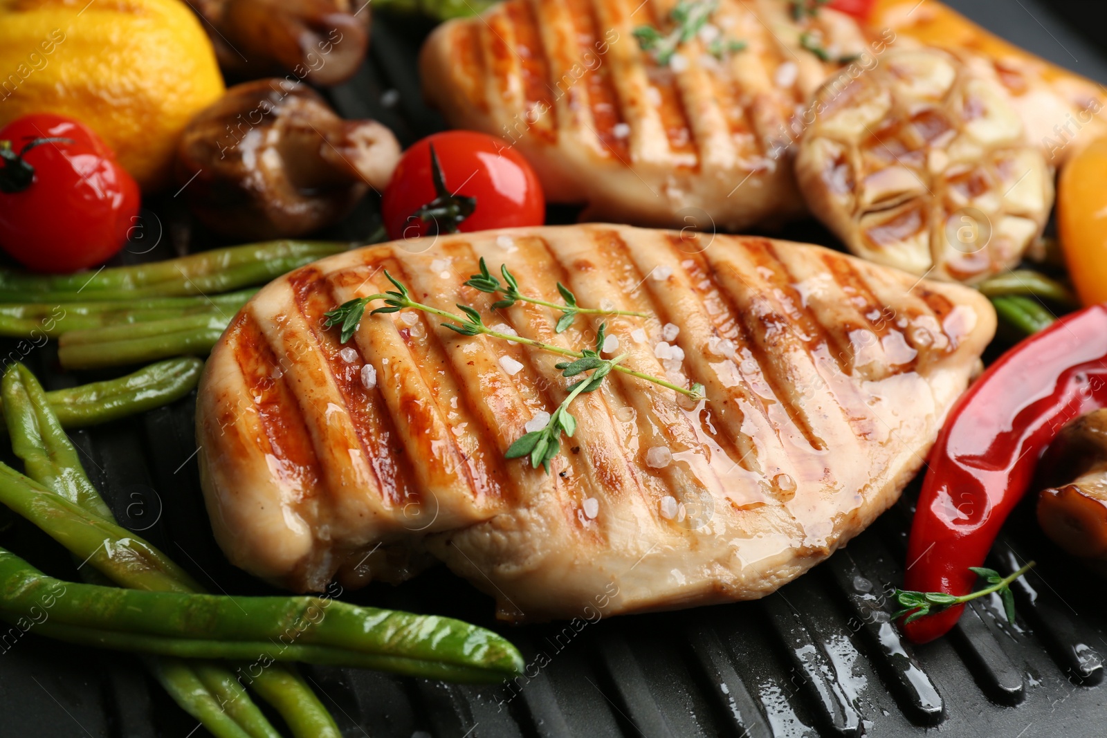 Photo of Tasty grilled chicken fillets with vegetables on frying pan, closeup