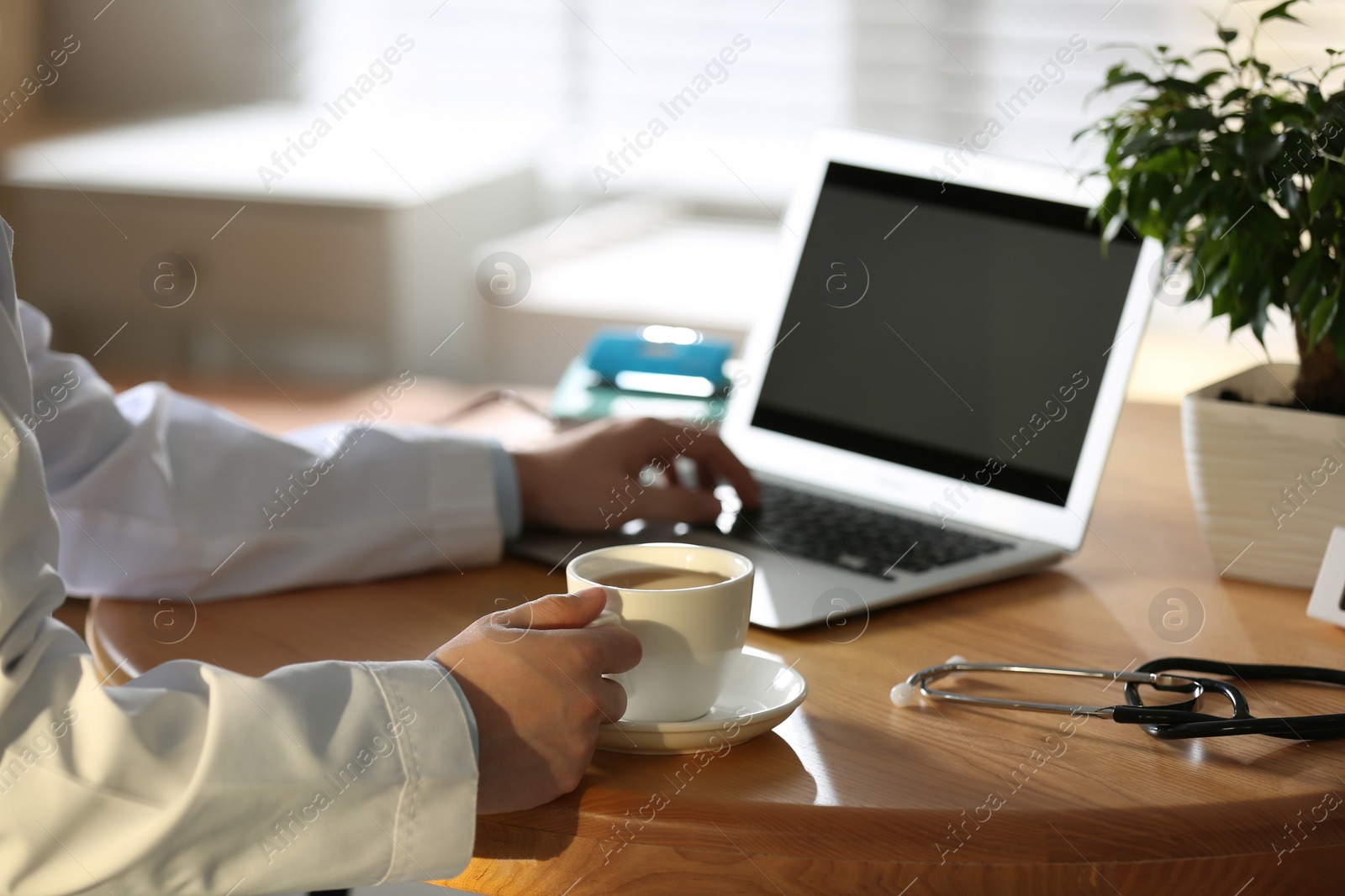 Photo of Professional doctor with cup of coffee working on laptop in office, closeup