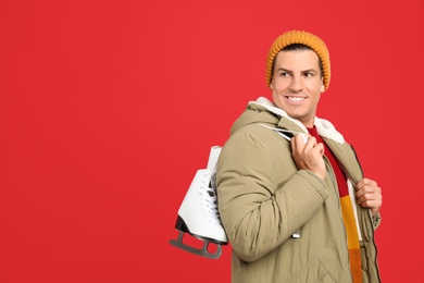 Photo of Happy man with ice skates on red background. Space for text