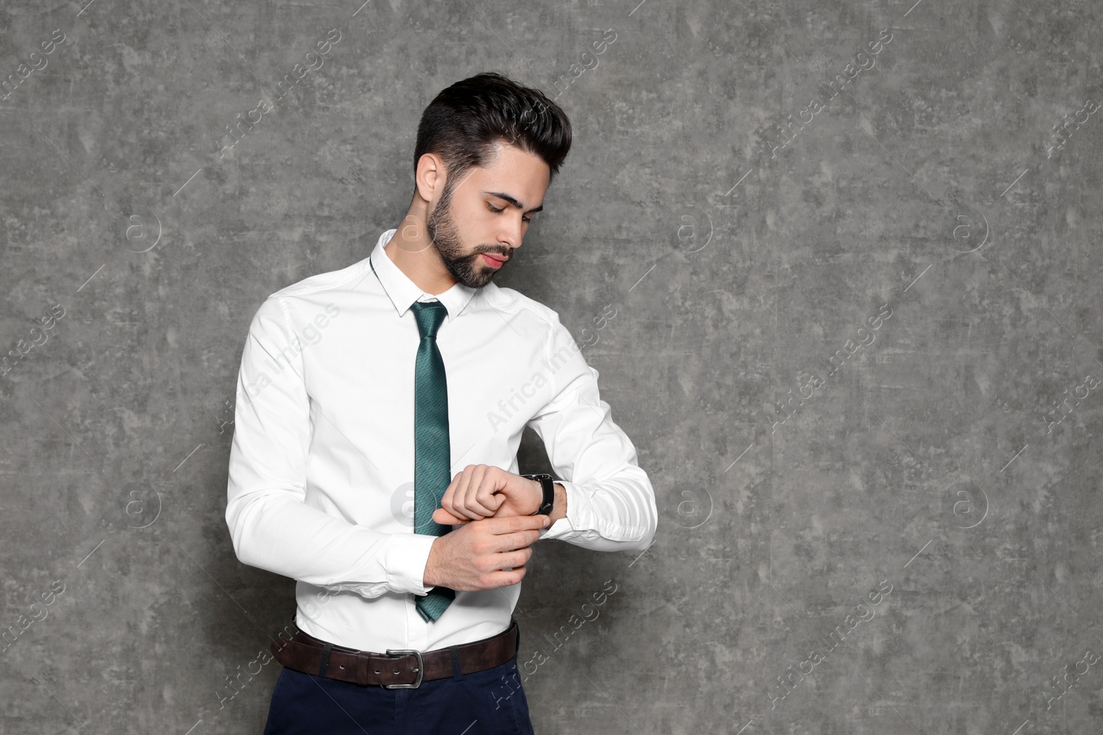 Photo of Portrait of confident businessman looking at wristwatch on grey background. Space for text