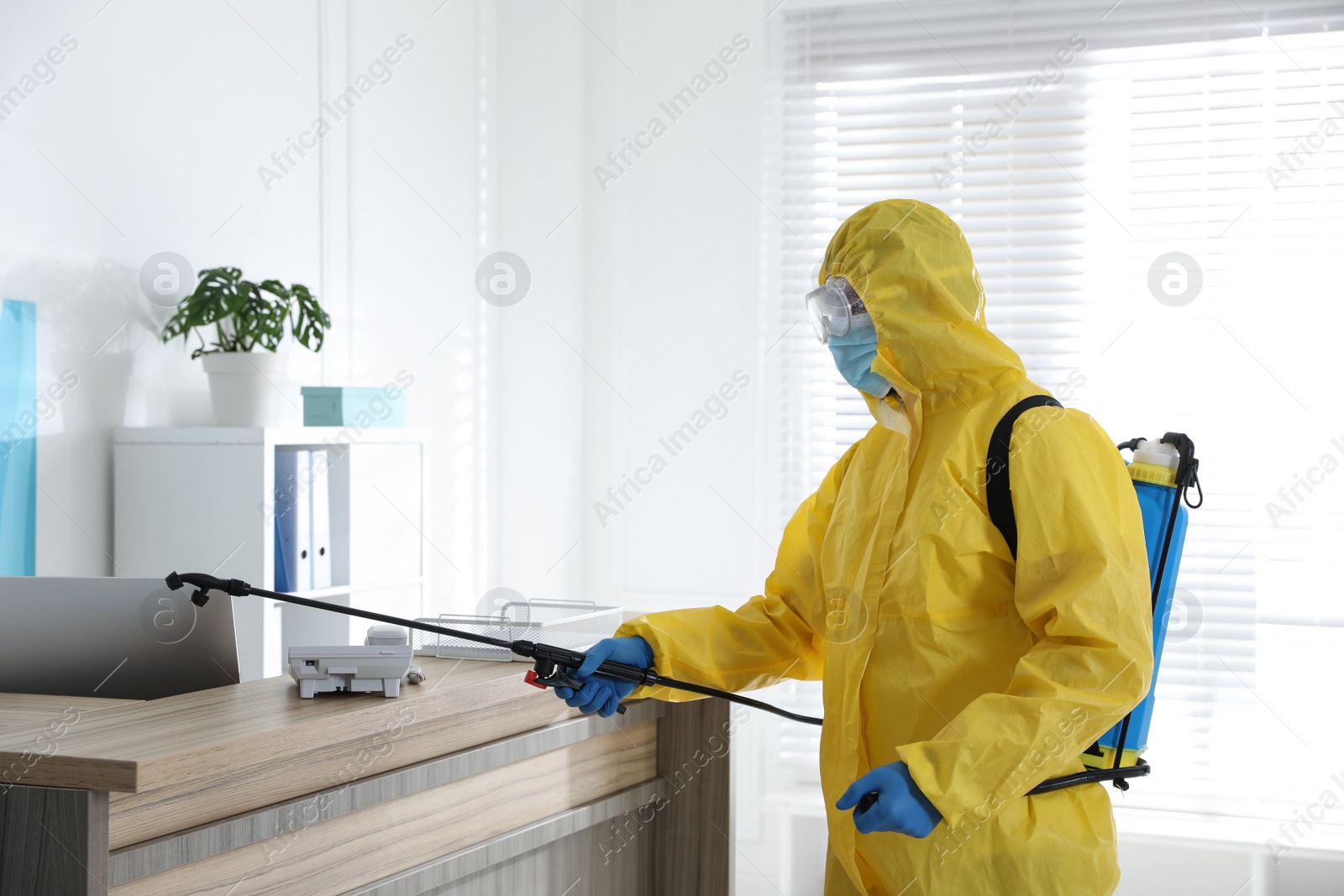 Photo of Employee in protective suit sanitizing office. Medical disinfection