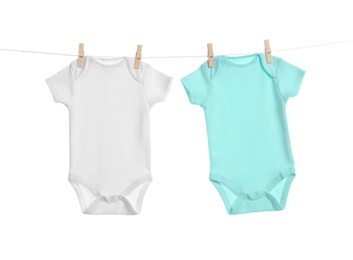 Colorful baby onesies hanging on clothes line against white background. Laundry day