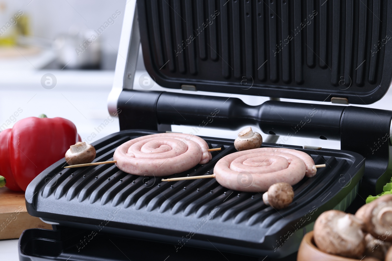 Photo of Electric grill with homemade sausages and mushrooms on table, closeup