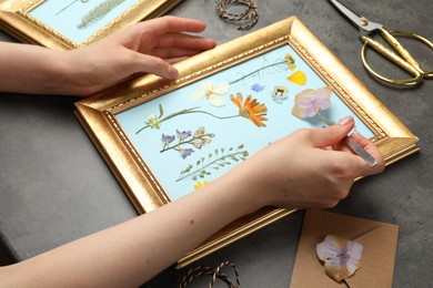 Photo of Woman making beautiful herbarium with pressed dried flower at black table, closeup