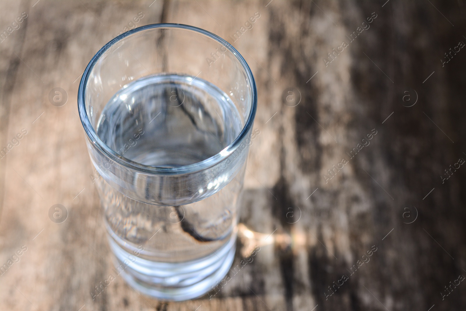Photo of Glass of water on wooden surface outdoors, closeup. Space for text