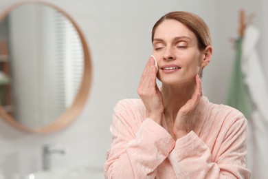 Photo of Beautiful woman removing makeup with cotton pad indoors, space for text